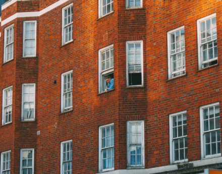 Woman looking outside a window of a block of flats